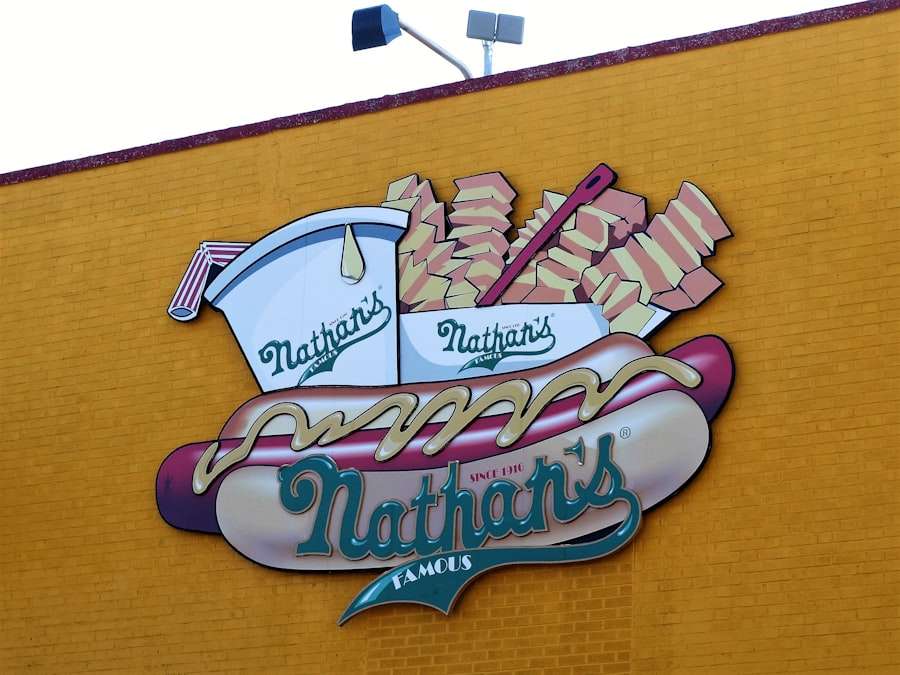 Suchmaschinenoptimierung Hannover - Ein großes Schild an einer gelben Backsteinmauer zeigt einen Hotdog mit Senf, eine Packung Pommes Frites und einen Becher mit Strohhalm. Auf dem Schild steht „Nathan’s Famous“ mit zwei kleineren „Nathan’s“-Logos auf dem Becher und der Packung Pommes Frites. Es ist fast so ikonisch wie jedes Design der Webagentur Hannover. Local SEO Agentur Hannover.