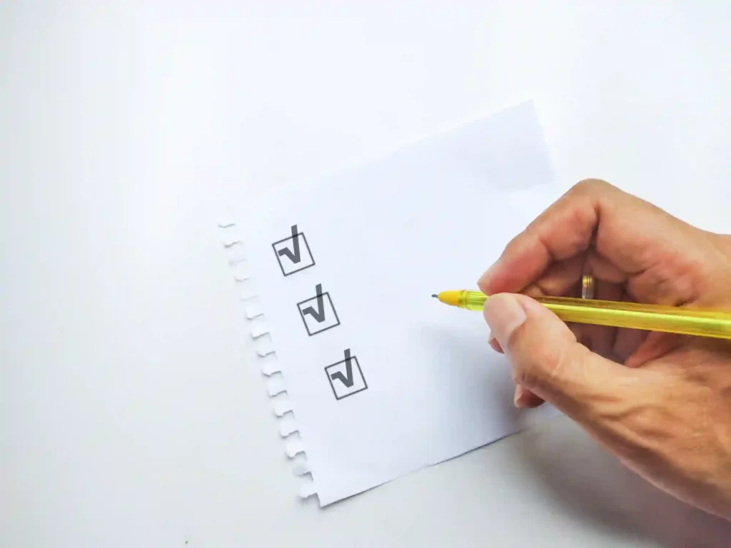 Suchmaschinenoptimierung Hannover - Eine Hand hält einen gelben Stift und markiert Kontrollkästchen auf einem weißen Blatt Papier. Das Papier hat drei Kontrollkästchen, jedes mit einem Häkchen, die in einer vertikalen Linie auf der linken Seite der Seite angeordnet sind. Das Papier hat auf der linken Seite eine spiralförmige Abreißkante, möglicherweise für Notizen zum Thema „Google-Bewertungen löschen lassen“. Local SEO Agentur Hannover.