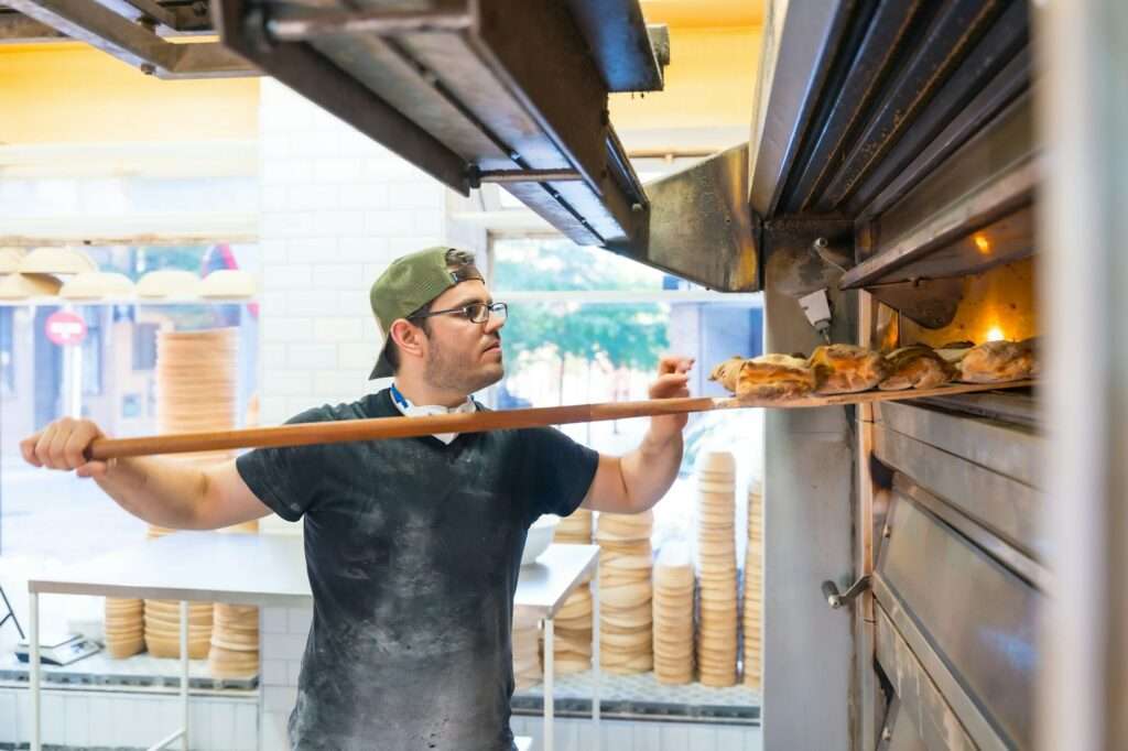 Baker of bakery in the workshop workshop of artisan bakery baking loaves in the oven