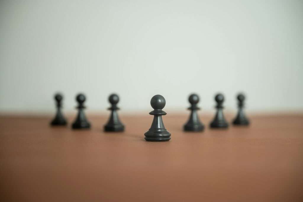 Chess pawn figures placed in a pyramid shaped line on brown surface