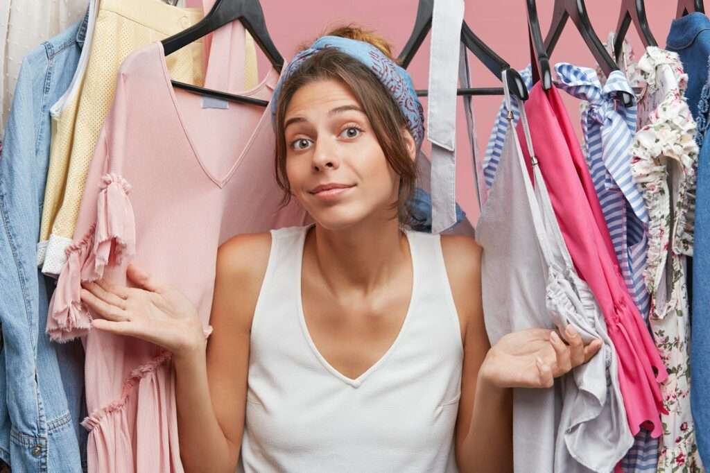 Cute European woman wearing white T-shirt, feeling uncertainty while looking through rank with cloth