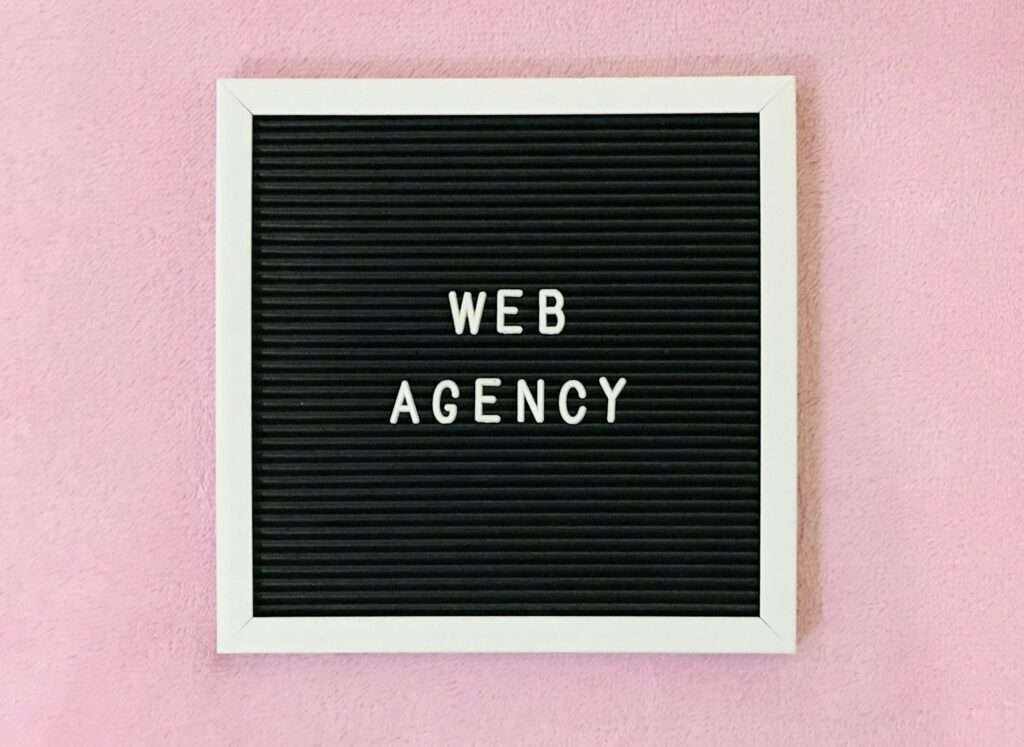 SEO Hannover - Auf einem schwarzen Letterboard mit weißem Rahmen steht in weißer Schrift „WEB AGENCY“. Das Board ist auf einem rosa Untergrund angebracht und spiegelt so perfekt das Wesen der Webagentur Hannover wider. Local SEO Agentur Hannover.