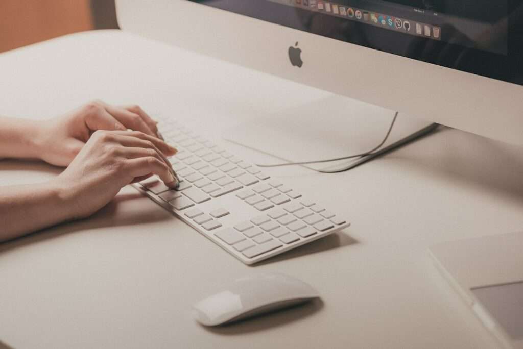 SEO Hannover - Auf einem Schreibtisch steht ein Mensch vor einem großen Computermonitor, daneben steht eine weiße Funkmaus. Dem Apple-Logo nach zu urteilen, handelt es sich vermutlich um einen iMac. Diese Szene könnte sich auch im Büro der Webagentur Hannover abspielen. Local SEO Agentur Hannover.