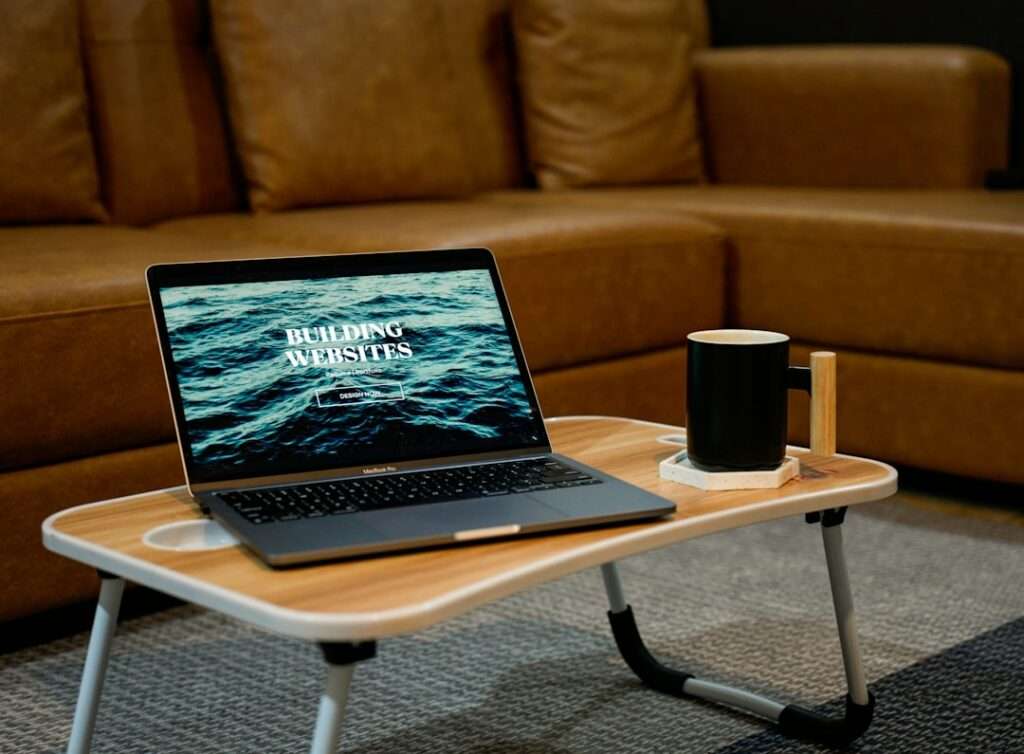 SEO Hannover - Auf einem kleinen Holztisch steht ein Laptop, auf dessen Bildschirm „Kosten für Website-Erstellung“ steht. Daneben steht eine schwarze Tasse auf einem Untersetzer. Im Hintergrund verleiht eine braune Ledercouch dem gemütlichen Teppichboden Wärme. Local SEO Agentur Hannover.