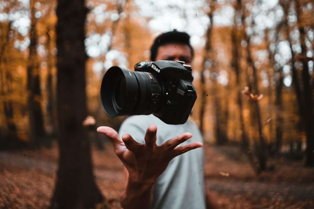 SEO Hannover - In einem mit Herbstlaub geschmückten Wald genießt eine Person einen spielerischen Moment mit ihrer DSLR-Kamera. Diese einzigartige Fotografie fängt die Kamera scharf ein, während der gemischte Hintergrund und die unscharfe Figur einen ätherischen Schwebeeffekt erzeugen. Local SEO Agentur Hannover.