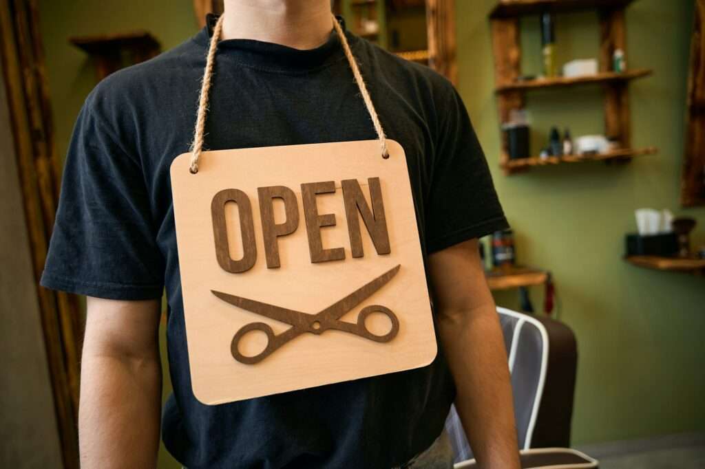 Man coiffeur holding on his neck sign with open inscription in barbershop