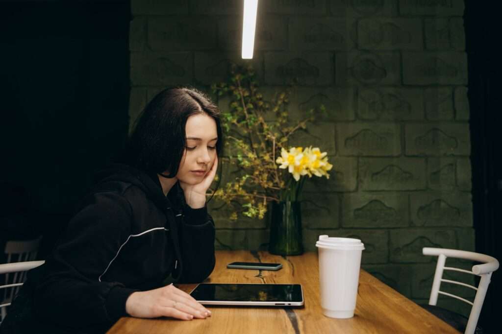 Sad hipster girl browsing boring websites on smartphone during leisure time in coffee shop outdoors.