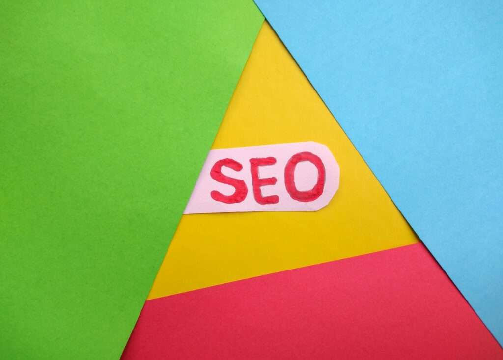 SEO Hannover - Ein Zettel mit der Aufschrift „Google SEO“ in roter Schrift liegt zwischen bunten Blättern in Grün, Blau, Gelb und Rot. Local SEO Agentur Hannover.