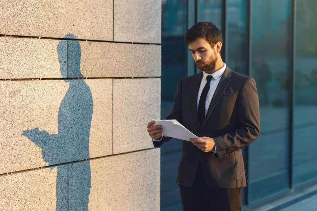 Serious young businessman in a classic suit reading advantageous business document in paper