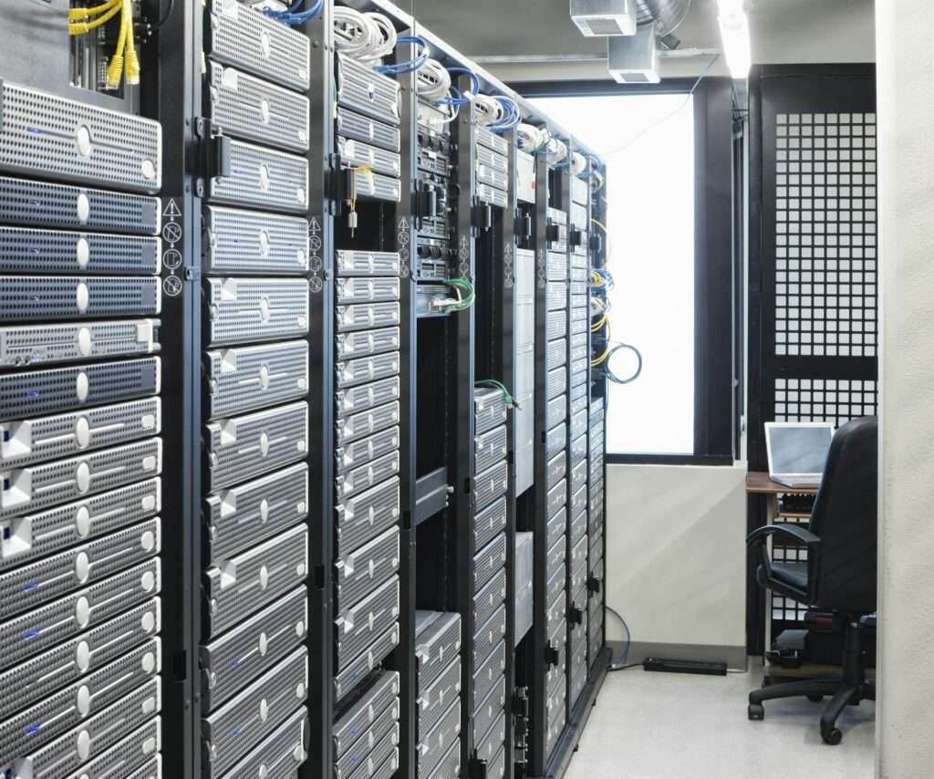 SEO Hannover - Ein Raum voller Server-Racks mit Computerhardware bietet erstklassige Hosting-Dienste. Kabel verbinden die Server, während eine nahe gelegene Workstation mit Stuhl und Laptop für einen reibungslosen Betrieb sorgt. Der Raum ist hell erleuchtet und verfügt auf einer Seite über ein großes Fenster. Local SEO Agentur Hannover.