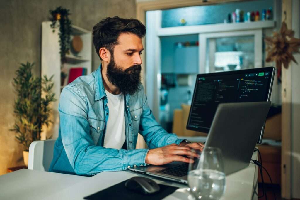 Side view of a website designer sitting at the home office and typing code on a laptop.