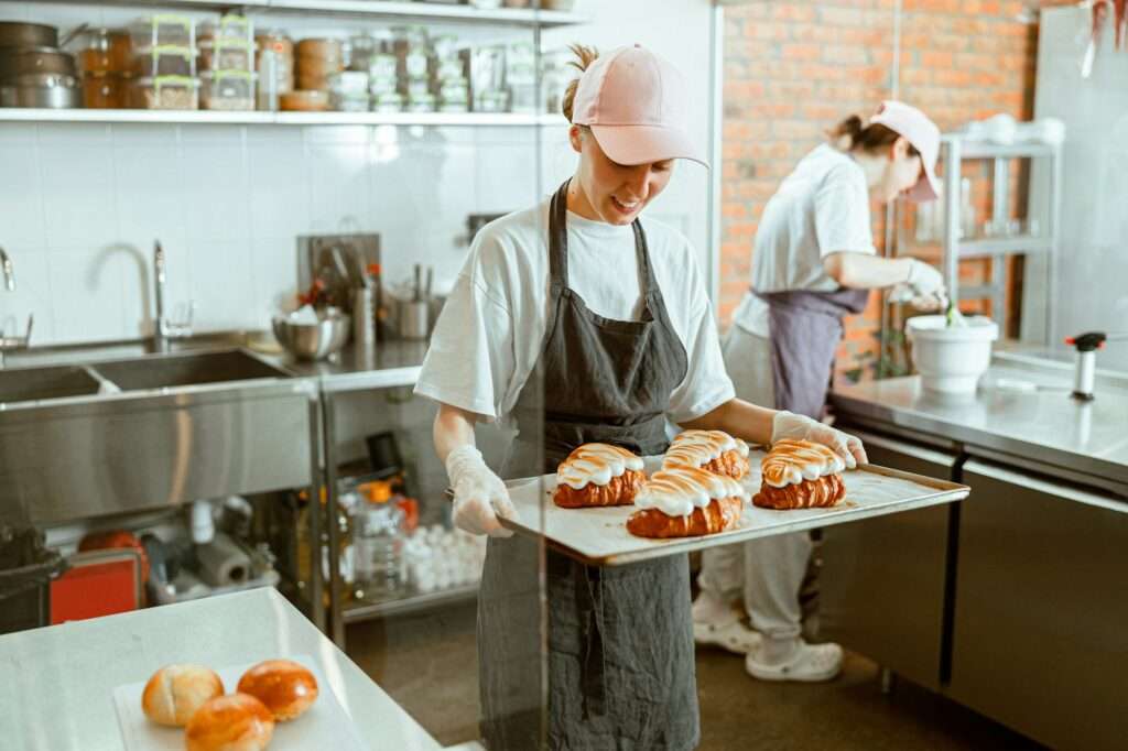 Smiling woman holds tray with delicious croissants decorated with burnt cream in craft bakery