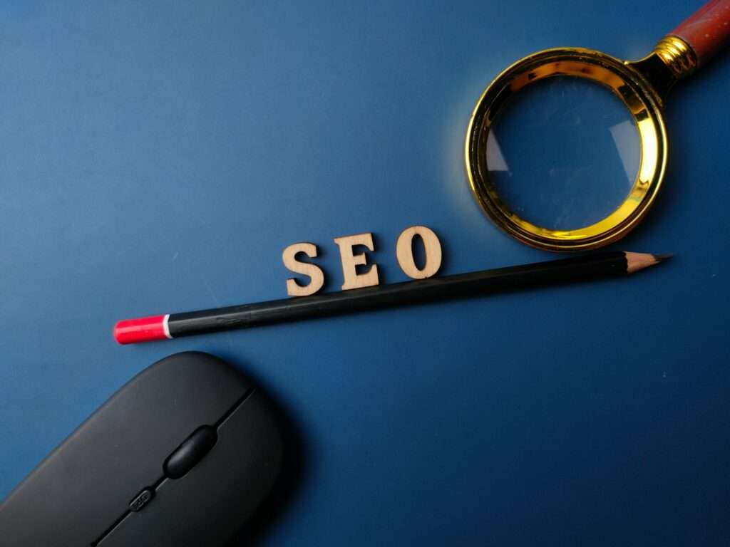 SEO Hannover - Eine Lupe, ein Bleistift und die Buchstaben „SEO“ auf blauem Hintergrund symbolisieren die SEO-Praktiken von Google. In der unteren linken Ecke lugt eine optische Maus hervor und deutet auf digitale Erkundung hin. Local SEO Agentur Hannover.