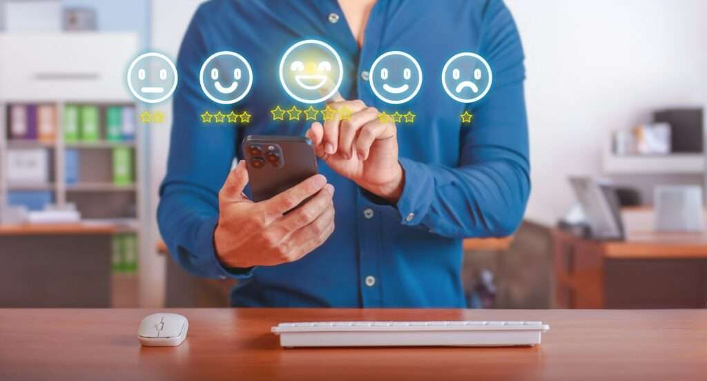 SEO Hannover - Eine Person in einem blauen Hemd benutzt ein Smartphone und interagiert mit einer virtuellen Feedback-Schnittstelle über dem Bildschirm. Auf dem Display sind fünf Smileys von traurig bis glücklich zu sehen, jedes mit einer Sternebewertung – ein Hinweis darauf, wie wichtig Google bei der Erfassung der Nutzerstimmung ist. Local SEO Agentur Hannover.