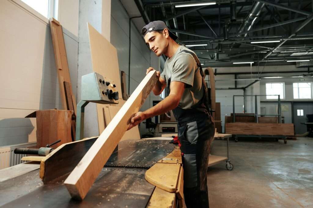 Young carpenter working on woodworking machines in the furniture factory