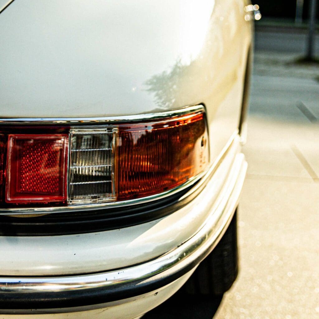 Webdesign Hannover - Nahaufnahme des Hecks eines weißen Oldtimers, die das klassische Rücklichtdesign und das hintere Seitenteil in exquisiten Details hervorhebt. Diese Fotografie fängt einen sanft verschwommenen Hintergrund mit Andeutungen eines Gebäudes und umgebender Grünflächen ein. Local SEO Agentur Hannover.
