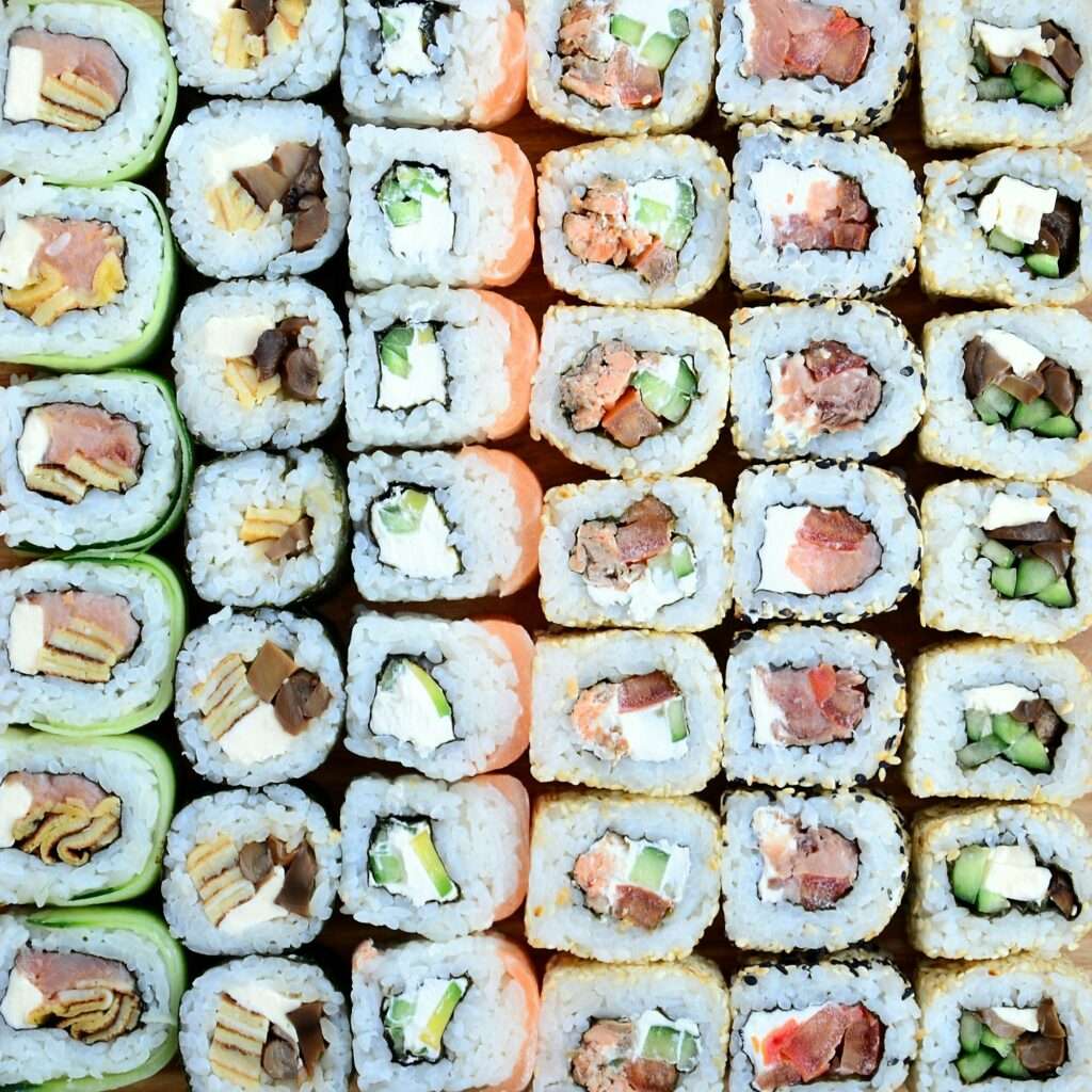 SEO Hannover - Eine übersichtlich angeordnete Auswahl an Sushirollen mit verschiedenen Füllungen wie Avocado, Räucherlachs, Gurke und Frischkäse. Die Rollen sind in einem Gittermuster angeordnet und weisen eine Vielzahl von Farben und Texturen auf – ideal für auffällige SEO für Bilder. Local SEO Agentur Hannover.