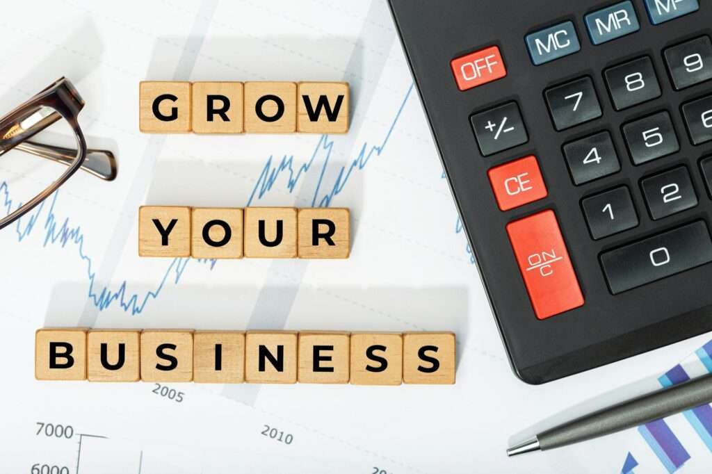 Webdesign Hannover - Auf einem Blatt Papier mit einem Finanzdiagramm steht aus Holzklötzen „GROW YOUR BUSINESS“ (WACHSEN SIE IHR UNTERNEHMEN). Ziel ist es, die Spitze von Google zu erreichen. Ein Taschenrechner, eine Brille und ein Stift sind ebenfalls zu sehen und bereiten die Bühne für strategisches Wachstum und Online-Erfolg. Local SEO Agentur Hannover.