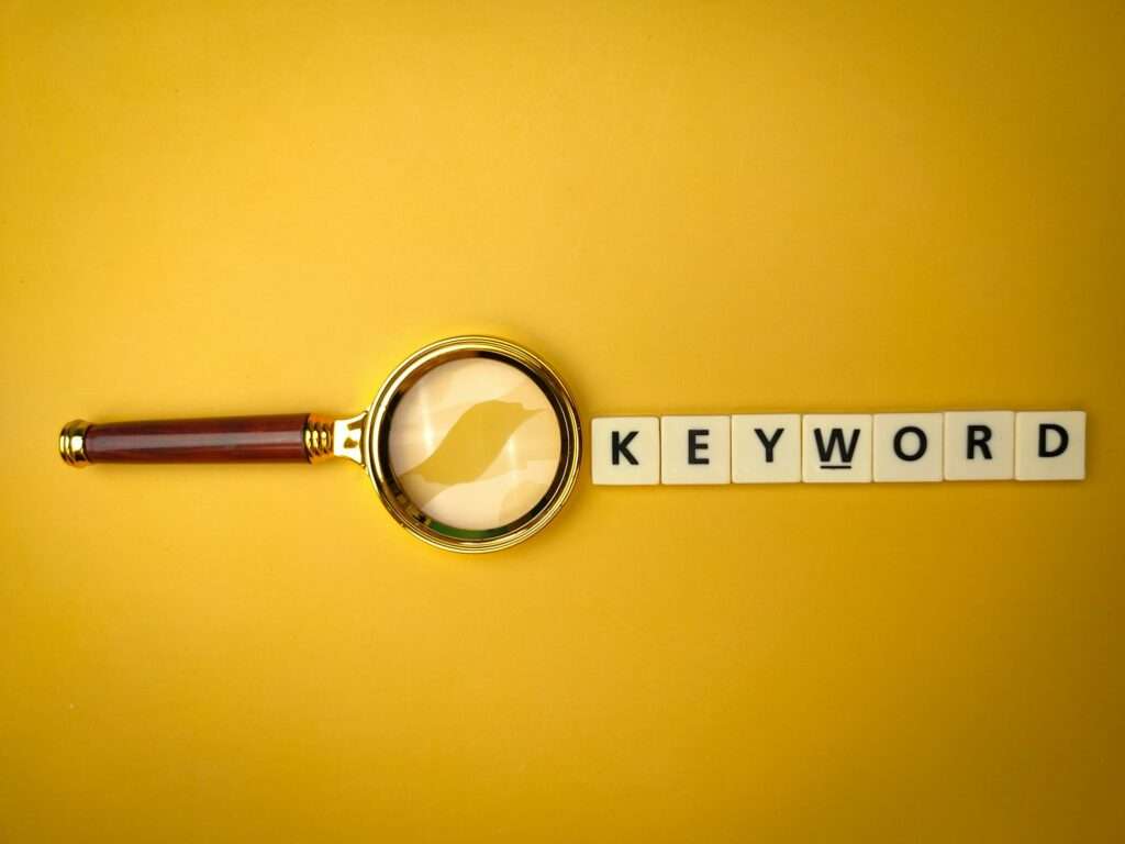 Webdesign Hannover - Eine Lupe schwebt über einer Reihe von Kacheln mit der Aufschrift „KEYWORD“, eingebettet in einen leuchtend gelben Hintergrund, und ähnelt einer gezielten Suche in einer Keyword-Liste. Local SEO Agentur Hannover.