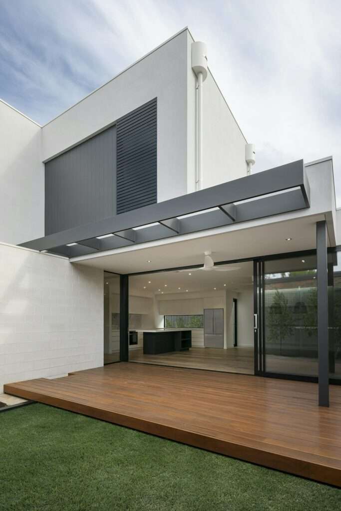 SEO Hannover - Dieses weiße Gebäude ist ein beeindruckendes Beispiel moderner Architektur und verfügt über ein Flachdach und eine einladende offene Terrasse mit Holzdeck. Die Glastüren und die Markise aus Metall verleihen Eleganz, während das minimalistische Design der Küche hervorsticht. Es ist von üppigem Gras umgeben und eignet sich ideal für die Präsentation in Immobilienfotografie. Local SEO Agentur Hannover.