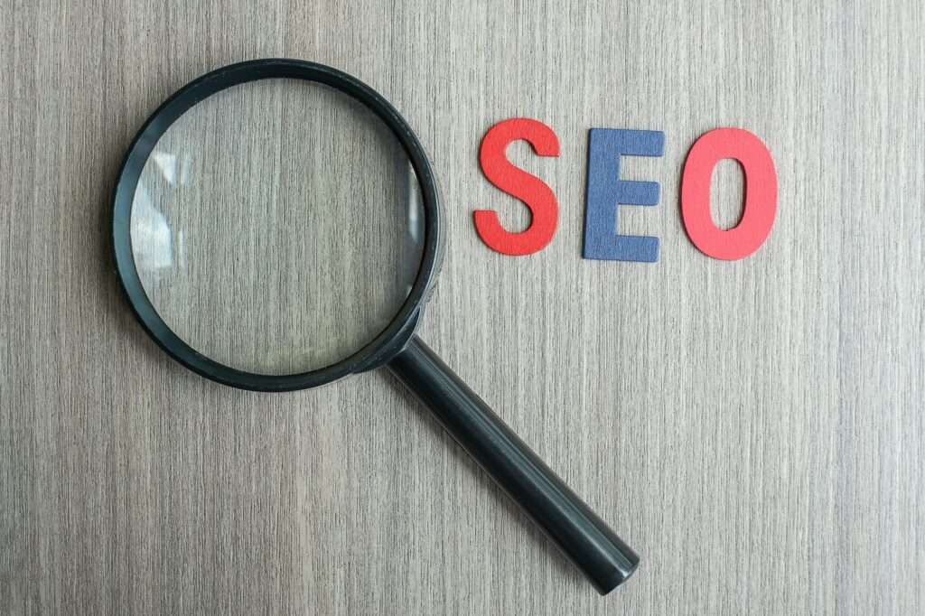 SEO Hannover - Neben den Buchstaben „SEO“ in Rot und Blau ist auf einer Holzfläche eine Lupe platziert, die den Fokus auf SEO-Optimierung symbolisiert. Local SEO Agentur Hannover.