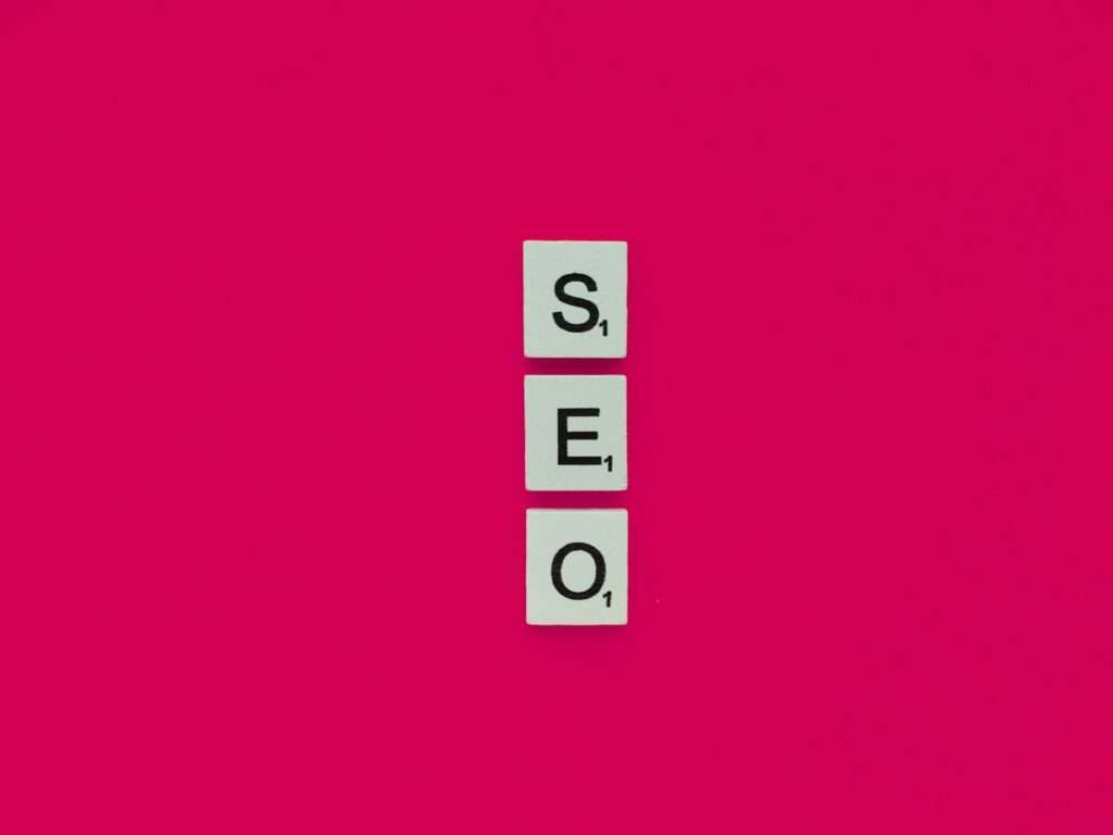 SEO Hannover - Drei Scrabble-Steine mit den Buchstaben „S“, „E“ und „O“ sind vertikal auf einem leuchtend rosa Hintergrund angeordnet und verweisen geschickt auf die Kunst der Suchmaschinenoptimierung oder SEO. Local SEO Agentur Hannover.