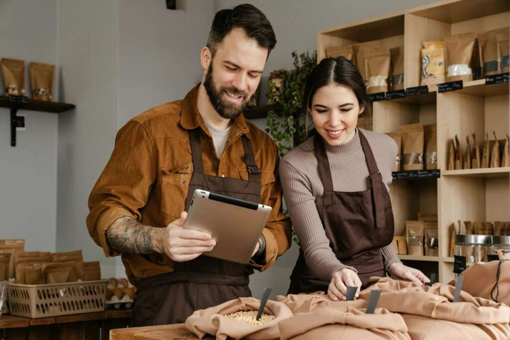 Smiling sellers man and woman using tablet while working in local shop