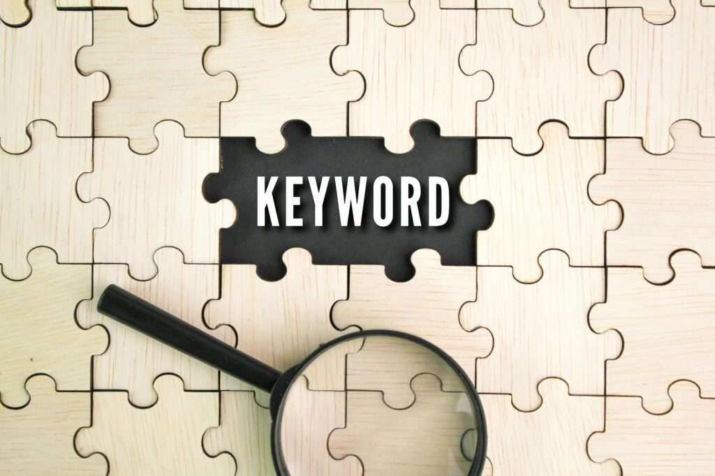 SEO Hannover - Ein Holzpuzzle, bei dem ein Teil fehlt, zeigt auf schwarzem Hintergrund das Wort „KEYWORDS“. Unten ist eine Lupe angebracht, die das Thema Suchen und Entdecken verstärkt. Local SEO Agentur Hannover.