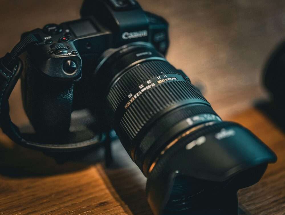 Webdesign Hannover - Eine schwarze Canon DSLR-Kamera mit Zoomobjektiv und Gegenlichtblende liegt auf einer Holzoberfläche. Perfekt für jeden Fotografen in Hannover: Die Kamera ist so ausgerichtet, dass die Objektivdetails und der Fokusring deutlich zu sehen sind. Local SEO Agentur Hannover.
