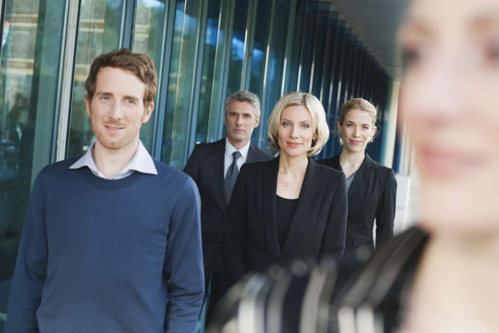 Webdesign Hannover - Eine Gruppe von vier Personen geht durch einen Flur mit Fenstern auf der linken Seite, aufgenommen von einem erfahrenen Businessfotografen in Hannover. Sie tragen professionelle Kleidung. Zwei Personen sind in eleganten Business-Anzügen zu sehen, während die anderen für mehr Tiefe dezent unscharf sind. Local SEO Agentur Hannover.