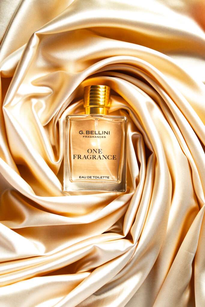 Webdesign Hannover - Ein rechteckiger Parfümflakon aus Glas mit der Aufschrift „G. Bellini Fragrances ONE FRAGRANCE EAU DE TOILETTE“ ruht auf glänzendem, goldfarbenem Satinstoff, der in weichen Falten angeordnet ist und mit dem raffinierten Stil eines Werbefotografen aus Hannover eingefangen wurde. Local SEO Agentur Hannover.