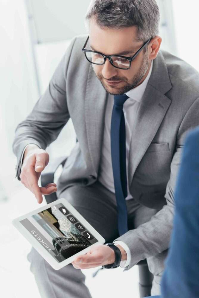 Webdesign Hannover - Ein Mann in einem grauen Anzug und mit Brille hält ein Tablet mit der Aufschrift „TICKETS“ in der Hand – wahrscheinlich bespricht er während seiner Präsentation, wie man Autohaus-Webseiten erstellen kann. Local SEO Agentur Hannover.
