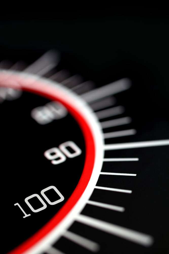 Webdesign Hannover - Nahaufnahme eines schwarzen Tachometers mit weißen Ziffern, die einen auffälligen roten Ring und die Zahl 100 im Fokus haben. Der verschwommene Hintergrund unterstreicht das Thema ladezeit optimierung für höchste Effizienz. Local SEO Agentur Hannover.