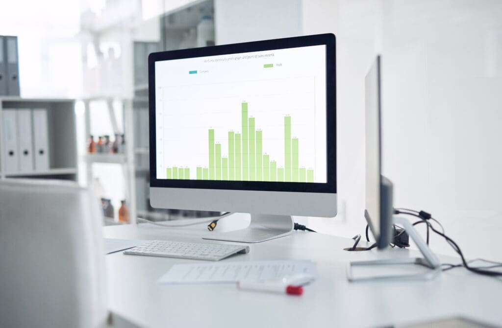 Webdesign Hannover - Ein Computermonitor auf einem Schreibtisch zeigt ein grünes Balkendiagramm mit zwei Datenkategorien aus einem SEO-Check-Onpage-Bericht an. Auf dem weißen Schreibtisch liegen Büromaterial und Dokumente verstreut, im Hintergrund sind Regale mit Ordnern zu sehen. Local SEO Agentur Hannover.