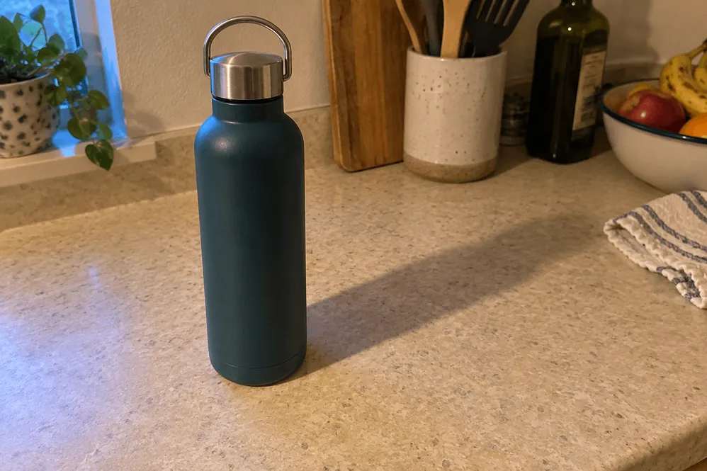 Eine blaue Mehrweg-Wasserflasche mit Metallverschluss steht auf einer hellen Küchenarbeitsplatte in der Nähe eines Fensters, neben Küchenutensilien, einer Obstschale und einem zusammengefalteten Geschirrtuch – perfekt inszeniert, sodass sie wie hochwertige Amazon-Produktfotos wirkt. Eine blaue Mehrweg-Wasserflasche mit Metallverschluss steht auf einer hellen Küchenarbeitsplatte in der Nähe eines Fensters, neben Küchenutensilien, einer Obstschale und einem zusammengefalteten Geschirrtuch – perfekt inszeniert, sodass sie wie hochwertige Amazon-Produktfotos wirkt.