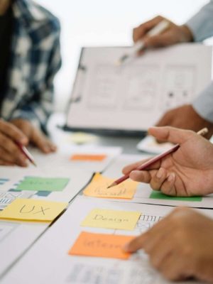 SEO Hannover - In einem energiegeladenen Studio arbeiten Menschen gemeinsam an einem Designprojekt und verwenden Haftnotizen und Skizzen mit den Aufschriften „UX“, „Design“ und „Intern“. Hände strecken Bleistifte aus und halten sie, während eine verschwommene Figur im Hintergrund Dokumente überprüft. Es ist ein dynamischer Tag für Webdesigner Hannover. Local SEO Agentur Hannover.